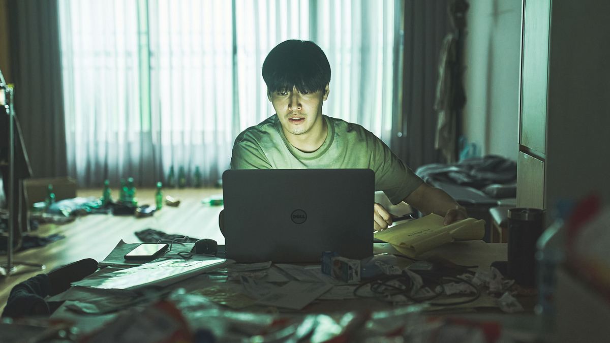 No Woo-sung sitzt vor seinem Laptop. Er ist umgeben von Müll, Briefen, Zeitschriften und Flaschen.