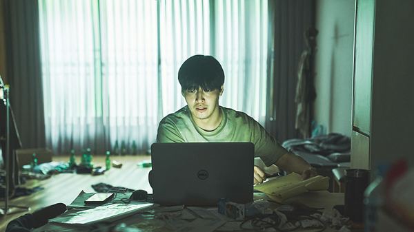 No Woo-sung sitzt vor seinem Laptop. Er ist umgeben von Müll, Briefen, Zeitschriften und Flaschen. - Foto: Young-Uk Jeon/Netlix