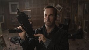 Schauspieler Bob Odenkirk verkörpert Nobody im gleichnamigen Film und hält eine automatische Waffe, einsatzbereit, hoch - Foto: IMDB