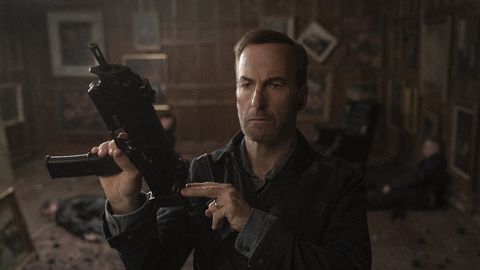 Schauspieler Bob Odenkirk verkörpert Nobody im gleichnamigen Film und hält eine automatische Waffe, einsatzbereit, hoch - Foto: IMDB