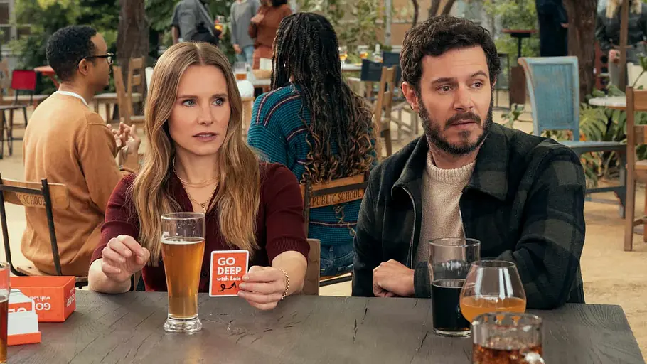 Das Paar Joanne und Noah aus „Nobody Wants This“ sitzt am Tisch mit Getränken vor sich und spielt ein Kartenspiel.
