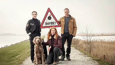 Das Team aus „Nord bei Nordwest“ steht mit einem Hund und einem Bombenwarnungsschild auf einem Deich. - Foto: NDR/Gordon Timpen Das Team aus „Nord bei Nordwest“ steht mit einem Hund und einem Bombenwarnungsschild auf einem Deich. - Foto: NDR/Gordon Timpen