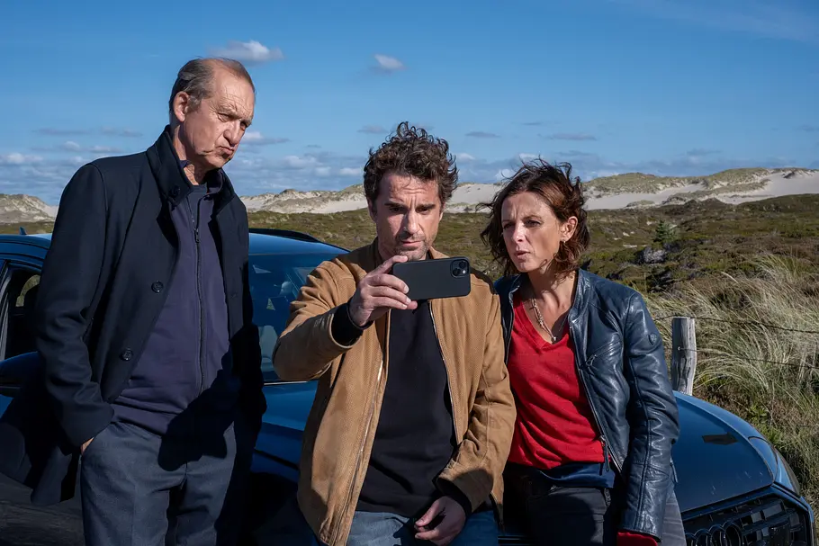 Nord Nord Mord - Sievers und der Gesang der Wale-Handlung Nord Nord Mord - Sievers und der Gesang der Wale: Carl Sievers (Peter Heinrich Brix), Hinnerk Feldmann (Oliver Wnuk) und Ina Behrendsen (Julia Brendler) stehen vor dem Auto und schauen Feldmanns Handy an.