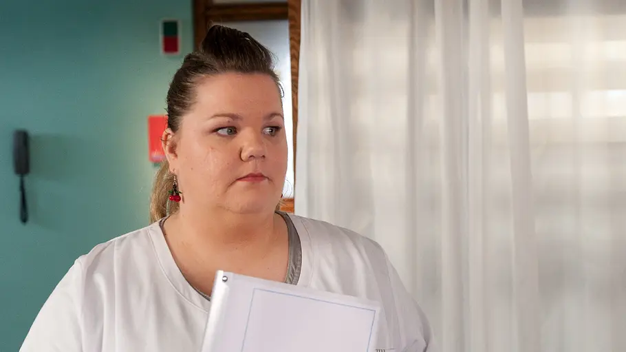 Manuela Wisbeck Frauke Prinz aus „Notruf Hafenkante“ steht in einem Krankenzimmer und hält eine Mappe mit der Aufschrift „Ein Plädoyer für die Organspende“ in den Händen. Sie blickt mit ernstem Gesichtsausdruck zur Seite.