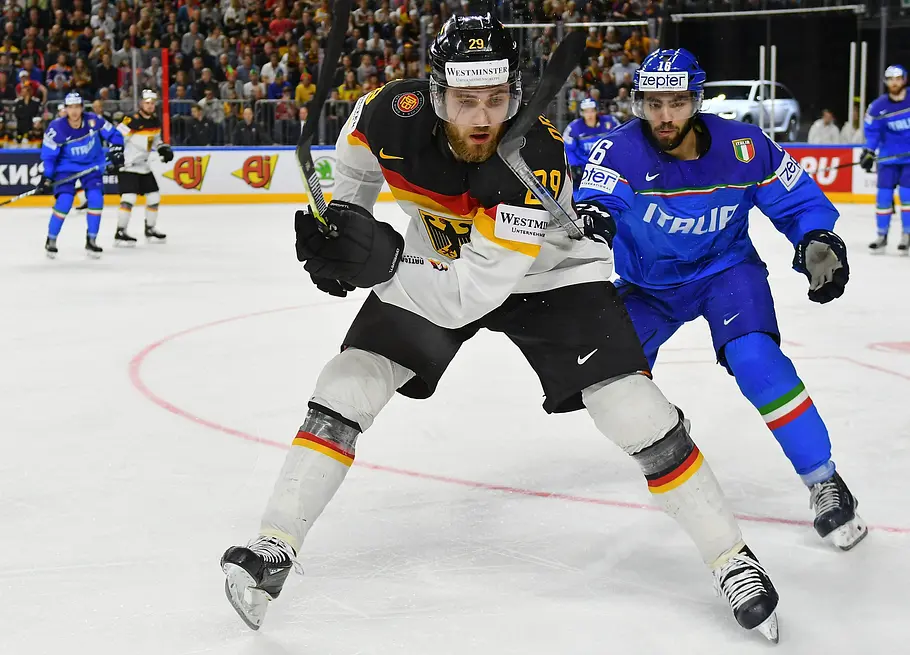 Deutscher Eishockey-Nationalspieler im Zweikampf mit einem italienischen Gegner während eines Länderspiels, dicht gefolgt vor vollbesetzten Rängen.