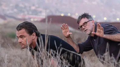 Leonardo DiCaprio schleicht durchs Gras, während er Anweisungen von Paul Thomas Anderson bekommt - Foto: © Photo Credit: Merrick Morton
