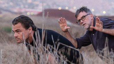 Leonardo DiCaprio schleicht durchs Gras, während er Anweisungen von Paul Thomas Anderson bekommt - Foto: © Photo Credit: Merrick Morton