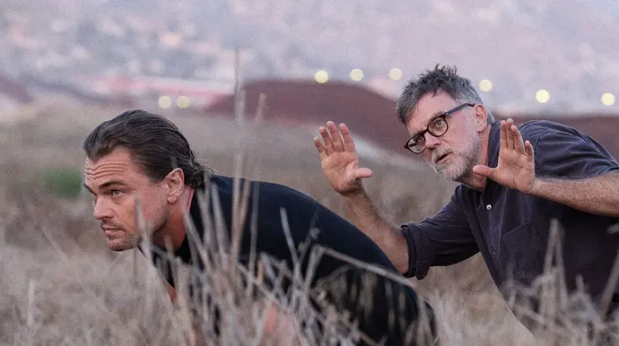 Leonardo DiCaprio schleicht durchs Gras, während er Anweisungen von Paul Thomas Anderson bekommt - Foto: © Photo Credit: Merrick Morton
