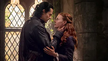 „Outlander: Blood of my Blood“: Brian Fraser und Ellen MacKenzie in einer Kirche. Er hält seine Hand an ihr Gesicht und die beiden schauen sich tief in die Augen. - Foto: Starz