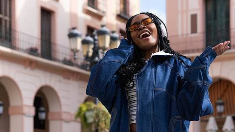 Frau mit Sonnenbrille und Over-Ear-Kopfhörer bewegt sich smooth über einen Marktplatz. - Foto: iStock / Alida Garcia