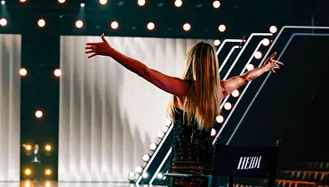 Heidi Klum steht mit dem Rücken zur Kamera und streckt begrüßen die Arme aus. - Foto: Seven.One Entertainment Group GmbH