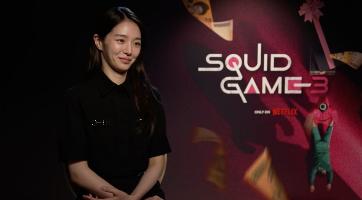 Park Gyu-young Park Gyu-young sitzt vor einem „Squid Game“-Poster und lächelt.