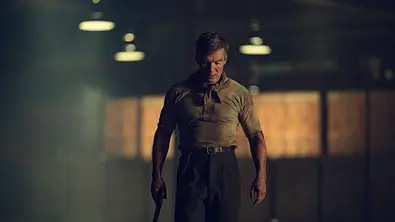 Tommy läuft mit einer Waffe durch eine Lagerhalle. - Foto: Netflix