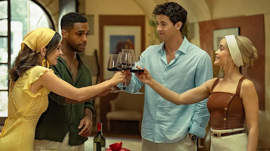 Vier junge Menschen stoßen lachend mit Rotweingläsern an einem gedeckten Tisch voller Snacks und Wein in mediterranem Ambiente an.