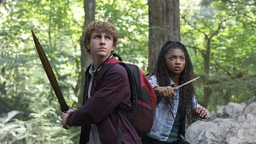 Percy Jackson und Annabeth Chase stellen sich mit Schwertern einer Gefahr in einem Wald. - Foto: Disney+