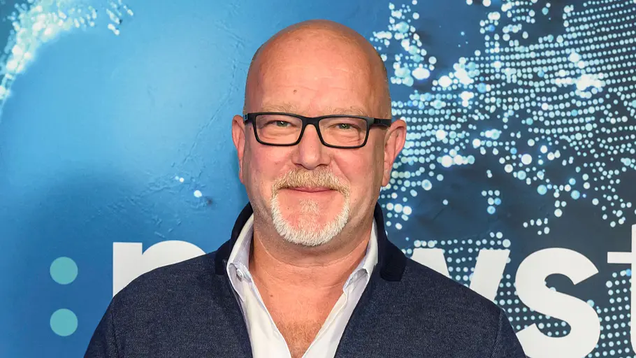 Urlaubstester Peter Giesel Peter Giesel mit Brille vor einer blauen Fotowand