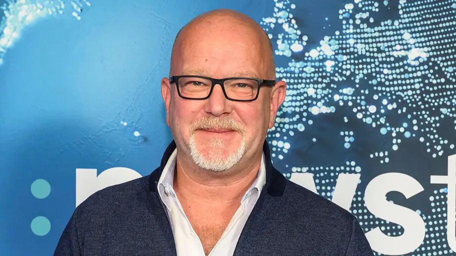 Peter Giesel ermittelt wieder gegen Urlaubsabzocke Peter Giesel mit Brille vor einer blauen Fotowand