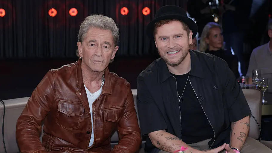 Peter Maffay und Johannes Oerding Peter Maffay in brauner Lederjacke und Johannes Oerding mit schwarzem Hut sitzen nebeneinander vor einem Tisch mit Blumen.