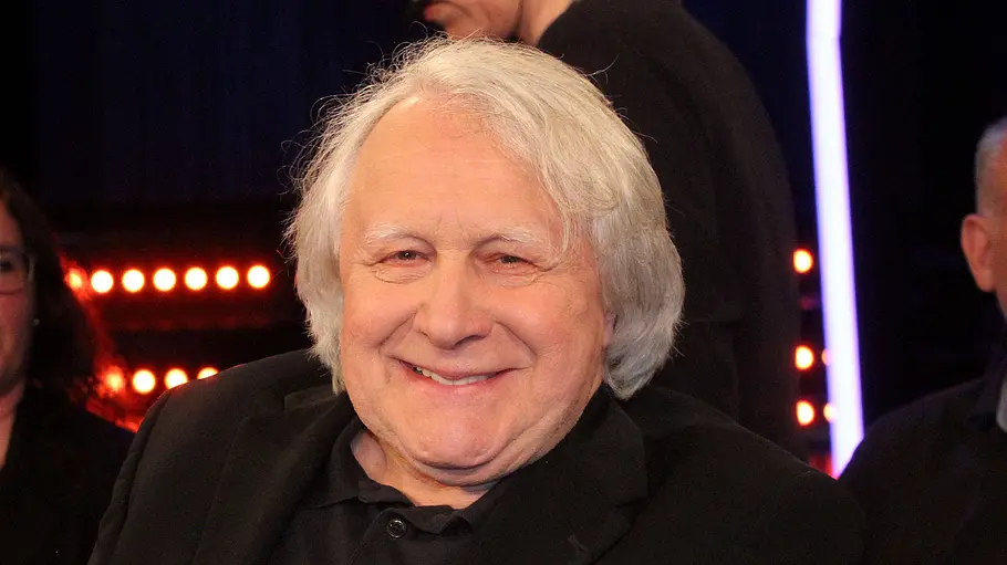 Peter Urban Abschied NDR Peter Urban in schwarzem Sakko sitzt lächelnd vor weiteren Personen und orangefarbenen Lichtreihen.