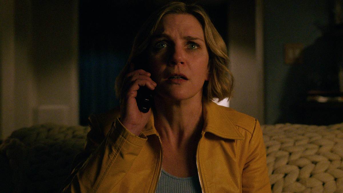 Rhea Seehorn sitzt auf einer Couch und hält sich ein Handy ans linke Ohr. Sie schaut entsetzt.