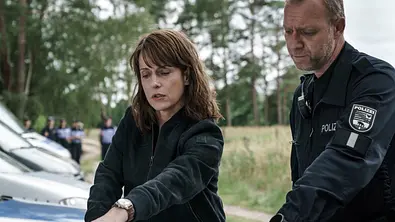 Claudia Michelsen steht als Ermittlerin Brasch neben einem weiteren Polizisten in der Natur. - Foto: MDR/filmpool fiction/Stefan Erhard Claudia Michelsen steht als Ermittlerin Brasch neben einem weiteren Polizisten in der Natur. - Foto: MDR/filmpool fiction/Stefan Erhard