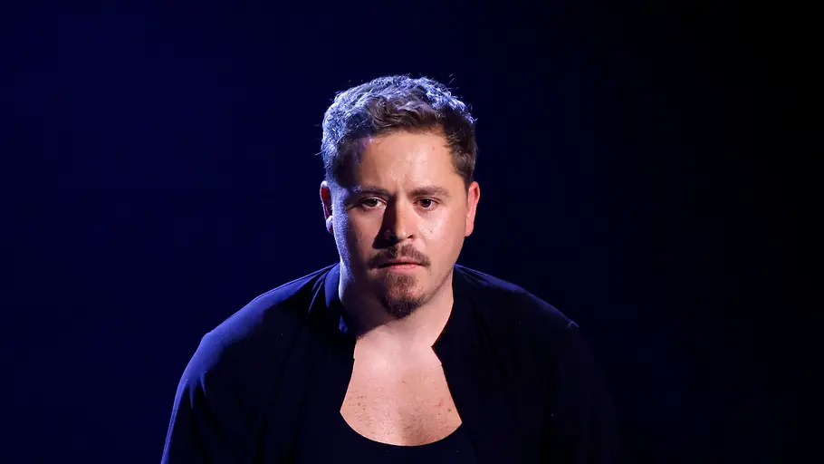 Gustav Schäfer im Porträt vor dunklem Hintergrund, gekleidet in schlichte schwarze Kleidung.