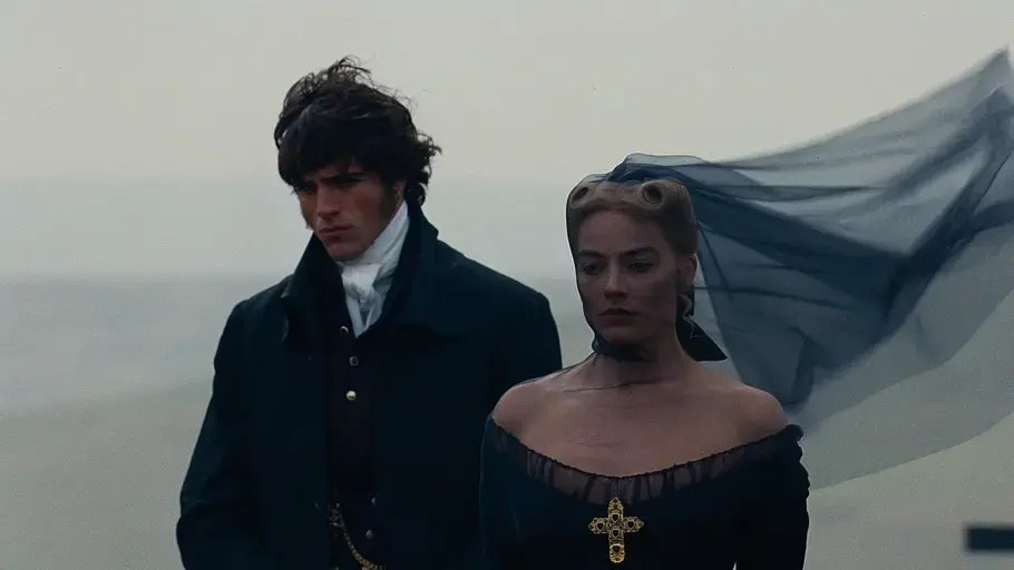 Jacob Elordi als Heathcliff und Margot Robbie als Cathy in „Wuthering Heights“ – Sturmhöhe: Ein Mann und eine Frau in dunkler, historischer Kleidung stehen an einem nebligen, windigen Ort. Der schwarze Schleier der Frau weht dramatisch im Wind, beide blicken ernst.
