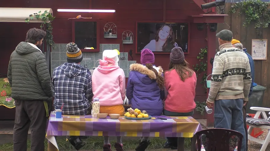 Die Promi Big Brother-Kandidaten sitzen mit dem Rücken zur Kamera im Garten. 