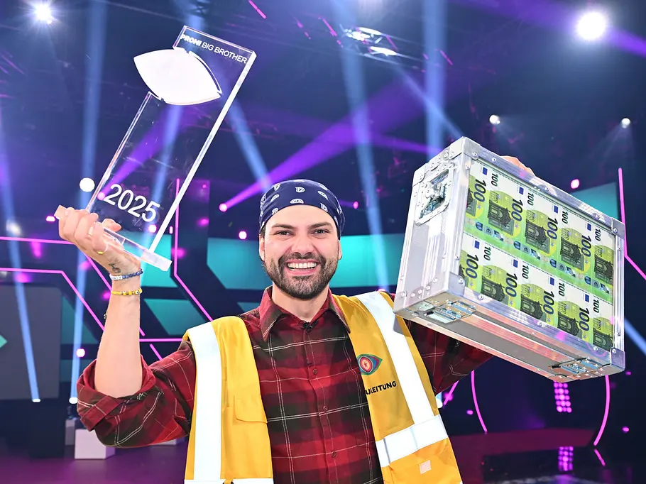 Promi Big Brother-Gewinner 2025 – Jimi Blue Ochsenknecht Jimi Blue Ochsenknecht hält lächelnd einen „Promi Big Brother“-Pokal 2025 und einen Koffer mit 100-Euro-Scheinen hoch.