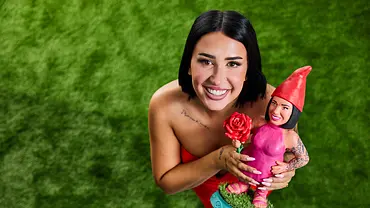 Francesca Morgese lächelt auf grünem Rasen in die Kamera und hält eine pink gekleidete Zwergenfigur mit roter Mütze und Rose. - Foto: Joyn/Marc Rehbeck Francesca Morgese lächelt auf grünem Rasen in die Kamera und hält eine pink gekleidete Zwergenfigur mit roter Mütze und Rose. - Foto: Joyn/Marc Rehbeck