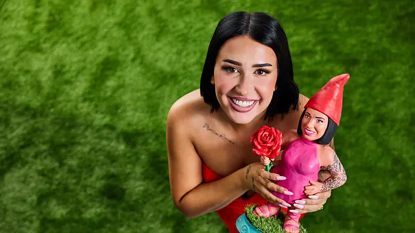 Francesca Morgese lächelt auf grünem Rasen in die Kamera und hält eine pink gekleidete Zwergenfigur mit roter Mütze und Rose. - Foto: Joyn/Marc Rehbeck Francesca Morgese lächelt auf grünem Rasen in die Kamera und hält eine pink gekleidete Zwergenfigur mit roter Mütze und Rose. - Foto: Joyn/Marc Rehbeck