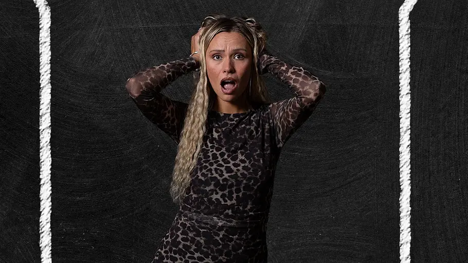 Anna Miltina Porträt einer Frau mit langen blonden Haaren vor einem schwarzen Hintergrund in Kreidetafel-Optik. Sie trägt ein langes, eng anliegendes Kleid mit Leopardenmuster und hält beide Hände an den Kopf. Mit weit geöffnetem Mund und überraschter Mimik blickt sie in die Kamera.