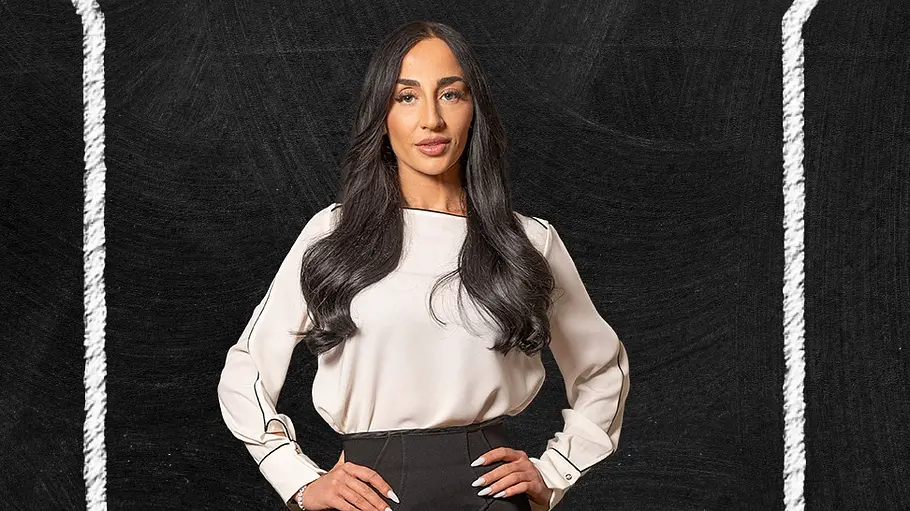 Melissa Porträt einer Frau mit langen dunklen Haaren vor einem schwarzen Hintergrund in Kreidetafel-Optik. Sie trägt eine weiße Bluse und einen schwarzen, figurbetonten Rock und posiert mit beiden Händen in der Hüfte.