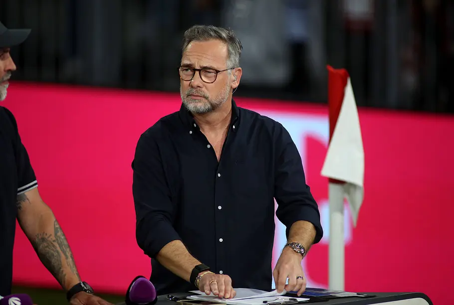 „Promi Padel WM“ 2026: Matthias Opdenhövel Matthias Opdenhövel steht mit Brille und dunklem Hemd an einem Tisch mit Papieren. Neben ihm steht eine rot-weiße Eckfahne.