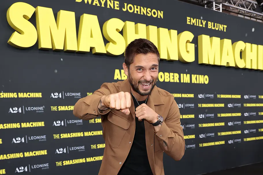 „Promi Padel WM“ 2026: Moritz Leitner Moritz Leitner posiert lächelnd in brauner Jacke mit erhobenen Fäusten vor einer Werbewand für „The Smashing Machine“.