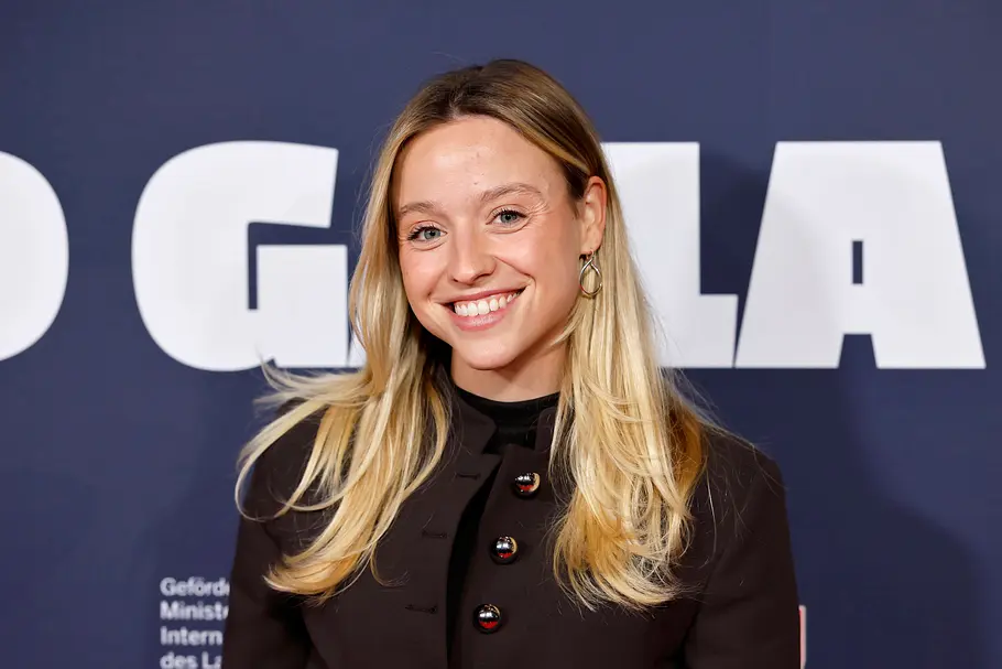 „Promi Padel WM“ 2026: Paula Enzweiler Paula Enzweiler lächelt mit langen blonden Haaren und schwarzer Jacke vor einem dunklen Hintergrund mit weißer Schrift.