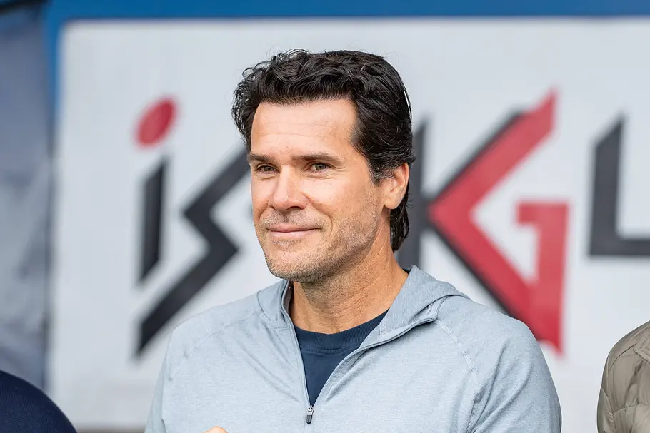 „Promi Padel WM“ 2026: Tommy Haas Tommy Haas trägt eine hellgraue Jacke über einem dunkelblauen Shirt und lächelt leicht vor einer Wand mit Schriftzug.