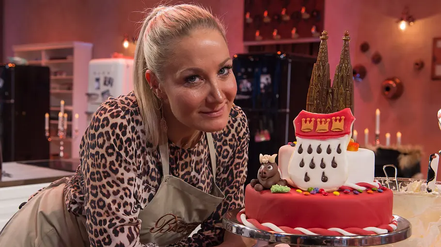 Janine Kunze Janine Kunze präsentiert in einer TV-Backshow stolz eine aufwendig dekorierte Torte mit Dom-Motiv in der Studioküche.
