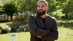 Aleks Petrovic steht mit verschränkten Armen in einem sonnigen Garten und blickt ernst zur Seite. Er trägt ein schwarzes Shirt und ein dunkles Sakko - Foto: RTL
