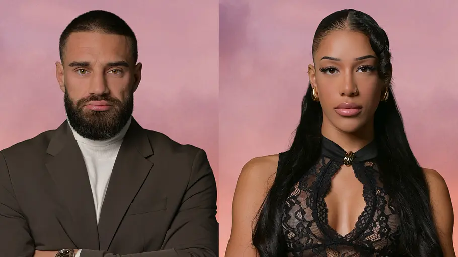 Aleks und Vanessa Ales und Vanessa im Porträt vor rosa Hintergrund, beide stehen mit verschränkten Armen und blicken ernst in die Kamera