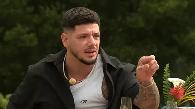 Gök mit Tattoos zeigt mit ausgestrecktem Finger nach vorn und hat einen emotionalen Gesichtsausdruck. Er sitzt draußen vor grünem Hintergrund. - Foto: RTL