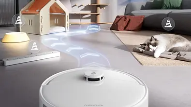 Ein runder Saugroboter fährt über den Boden eines Wohnzimmers, während eine Katze auf einer Matte neben einem Sofa schläft. Im Hintergrund stehen ein kleines Katzenhaus, ein Kratzbaum und eine Steckdosenleiste, über dem Boden ist eine grafisch dargestellte Fahrroute eingeblendet. - Foto: Amazon/PR Ein runder Saugroboter fährt über den Boden eines Wohnzimmers, während eine Katze auf einer Matte neben einem Sofa schläft. Im Hintergrund stehen ein kleines Katzenhaus, ein Kratzbaum und eine Steckdosenleiste, über dem Boden ist eine grafisch dargestellte Fahrroute eingeblendet. - Foto: Amazon/PR
