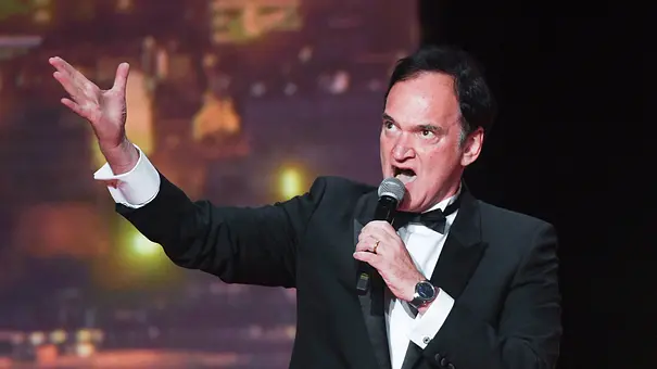 Quentin Tarantino steht im Anzug auf einer Bühne und spricht in ein Mikrofon. - Foto:  IMAGO / ABACAPRESS