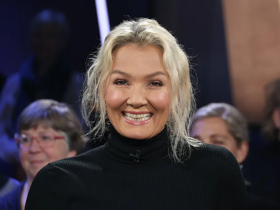 Quiz-Champion: Österreich-Deutschland-Special mit Franziska van Almsick Franziska van Almsick lächelt in einem schwarzen Rollkragenpullover in die Kamera. Hinter ihr sitzen mehrere Personen.