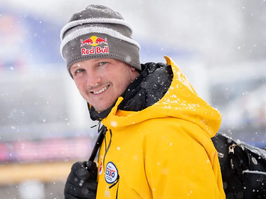 Quiz-Champion: Österreich-Deutschland-Special mit Thomas Morgenstern Thomas Morgenstern lächelt im Schneefall mit grauer Red-Bull-Mütze, gelber Winterjacke und schwarzem Rucksack in die Kamera.