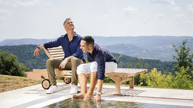 Ralf Schumacher und sein Freund Etienne Bousquet-Cassagne sitzen am Pool auf einer Liege.  - Foto: IMAGO / HANZA MEDIA
