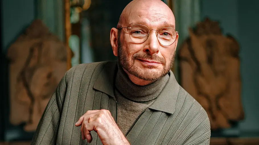 Ralph Morgenstern ist Schauspieler. Ralph Morgenstern schmunzelnd und mit erhobener Hand.