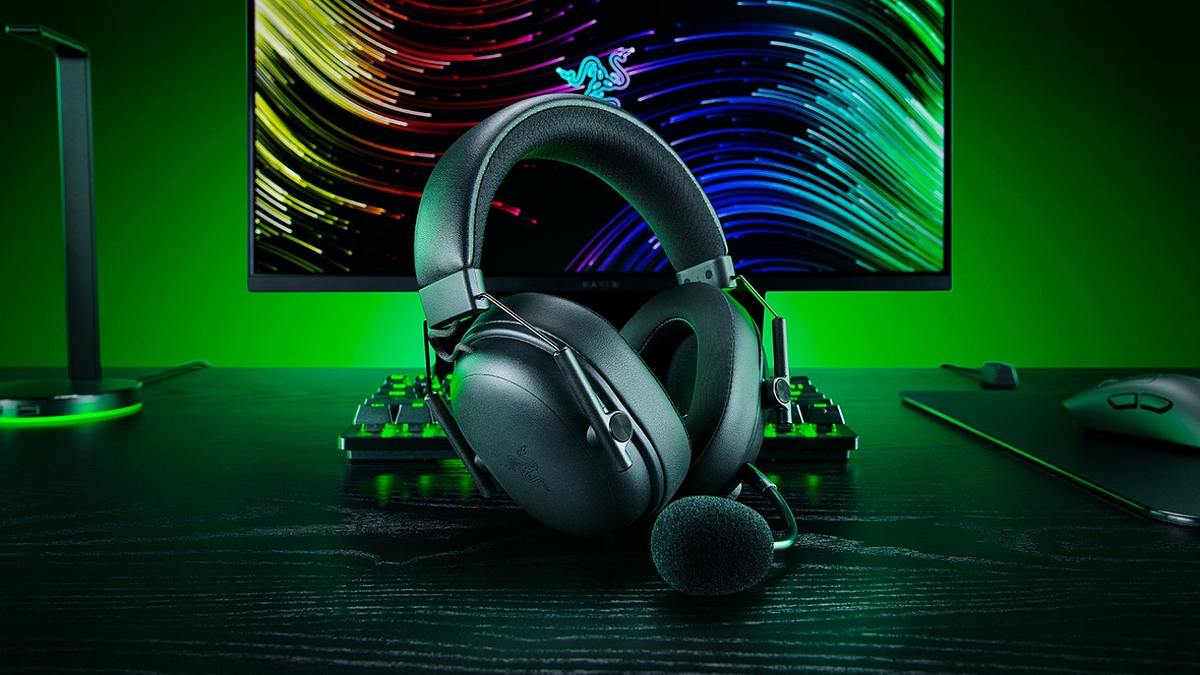 Ein Headset der Razer BlackShark V3-Serie im Vordergrund, dahinter mehr Razer-Zubehör vor einem Monitor mit grüner Hintergrundbeleuchtung.