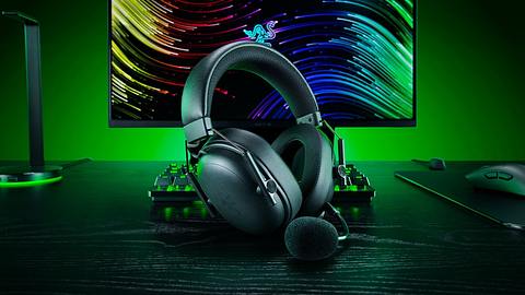 Ein Headset der Razer BlackShark V3-Serie im Vordergrund, dahinter mehr Razer-Zubehör vor einem Monitor mit grüner Hintergrundbeleuchtung. - Foto: © 2025 Razer Inc.
