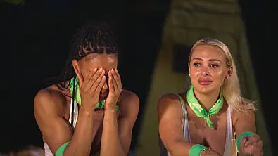 Zwei Kandidatinnen von „Reality Queens“ mit grünen Halstüchern sitzen nebeneinander, eine verdeckt emotional ihr Gesicht mit den Händen. - Foto: RTL